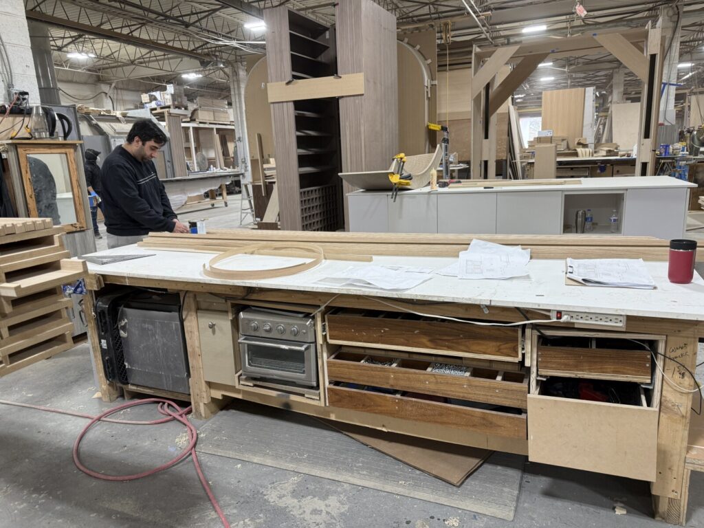 A craftsman working at a professional woodworking bench in a large furniture manufacturing facility.