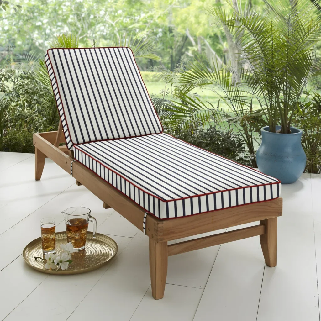 Outdoor wooden lounge chair with striped cushions and red piping in a garden setting