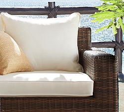 Outdoor wicker chair with a light sunbrella seat cushion in a bright garden setting.