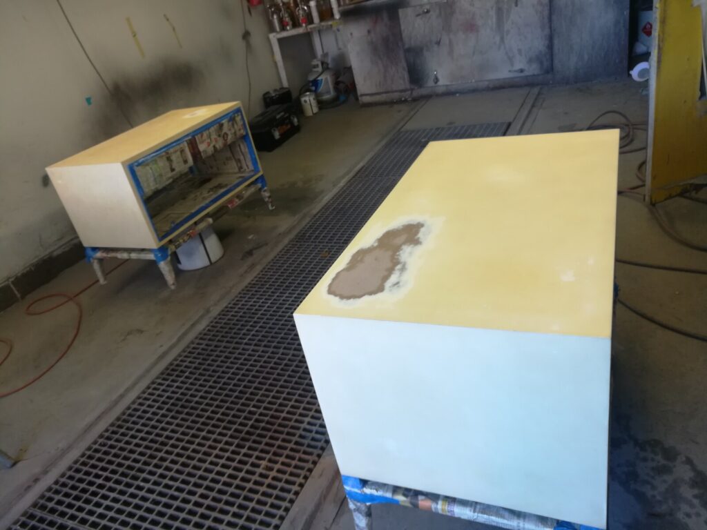 Custom white‑lacquer Barbara Barry bedside table in the spray room during the refinishing process.