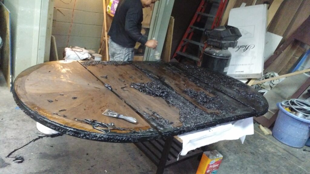 Wood dining table in the workshop as the top is being stripped during the refinishing process.