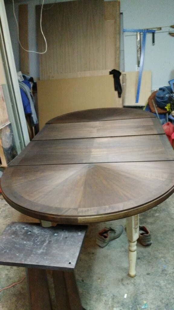 Wood dining table fully stripped to bare wood in the workshop, ready for sanding and finishing.