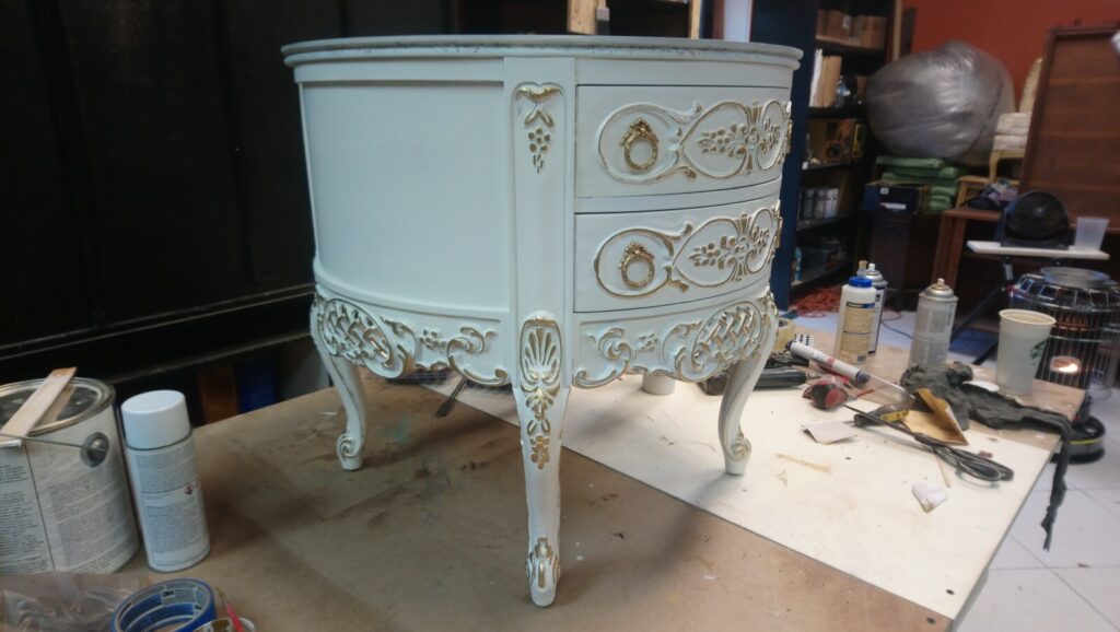 Antique carved side table fully restored with gold leaf detailing, photographed in the workshop after refinishing.