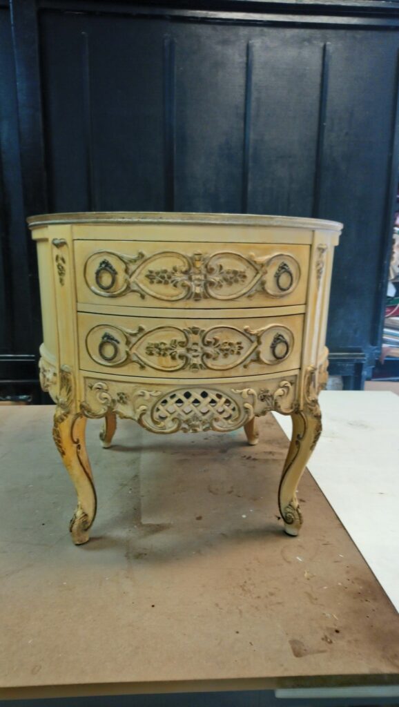 Antique carved side table in the workshop before refinishing, showing its worn finish and surface damage.