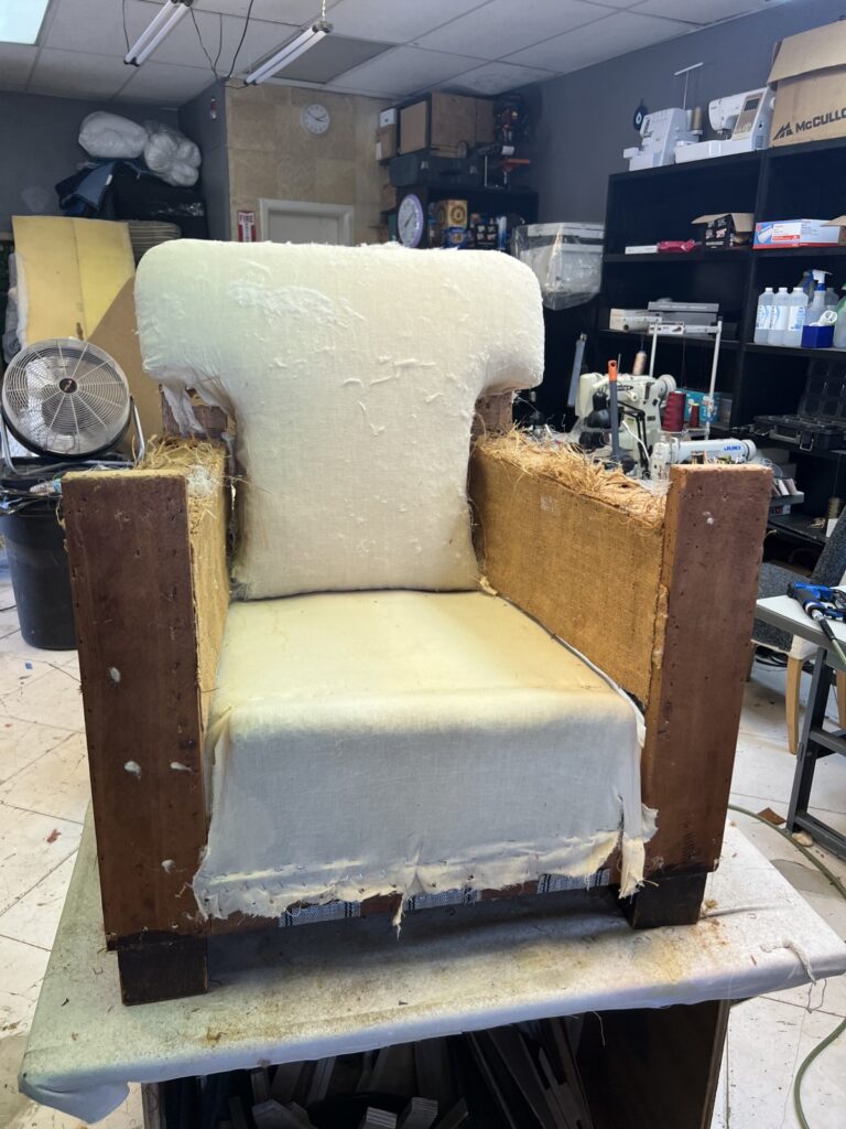 Antique club chair stripped down in the workshop before reupholstery, showing the exposed frame and springs.