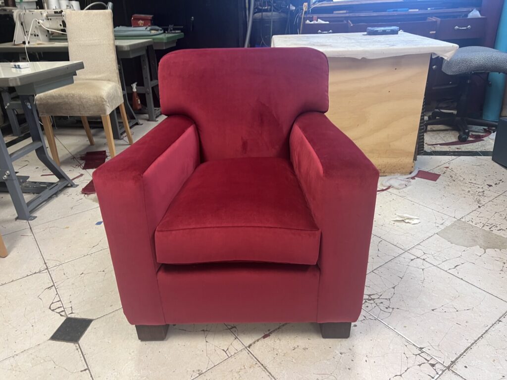 Antique club chair fully restored and reupholstered in red velvet, photographed in the workshop after completion.