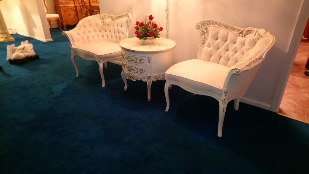 Pair of antique white chairs and a matching center table with gold leaf detailing, photographed in the client’s home after restoration.