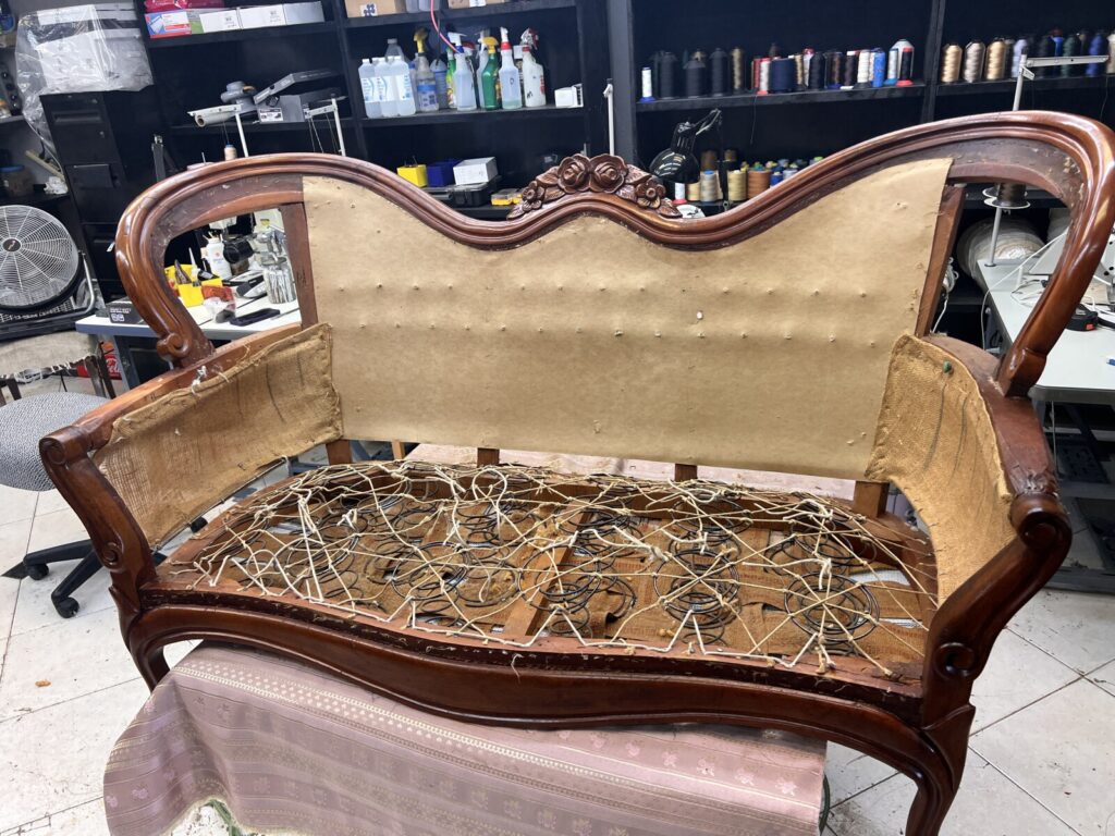 Antique Victorian settee in the workshop before restoration, showing structural repair work in progress.