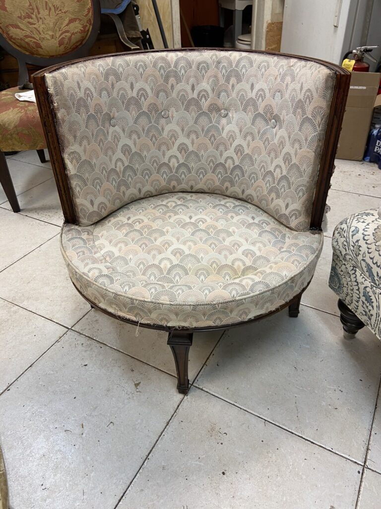 Antique barrel chair stripped down in the workshop before reupholstery, showing the exposed frame.