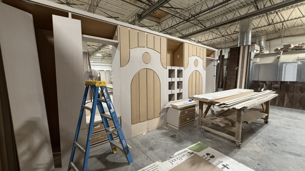 Detailed view of bare wood bed frames and a wall panel template with hand-drawn geometric arched patterns.