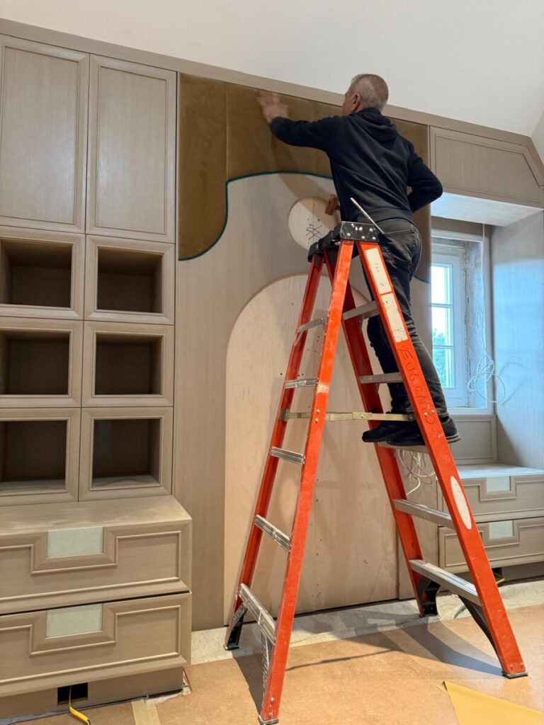 Progress shot of a specialist hand-installing velvet arched panels into the custom wall unit on-site.