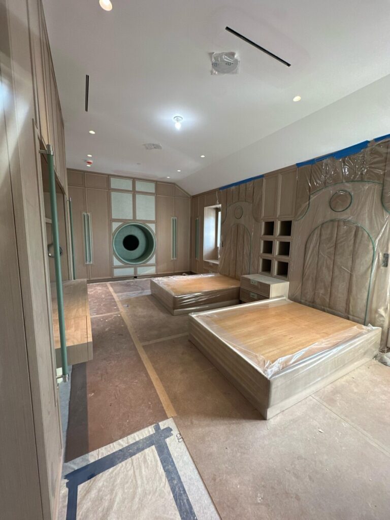 Installed wall panels and custom bed frames covered in protective plastic during final room construction.
