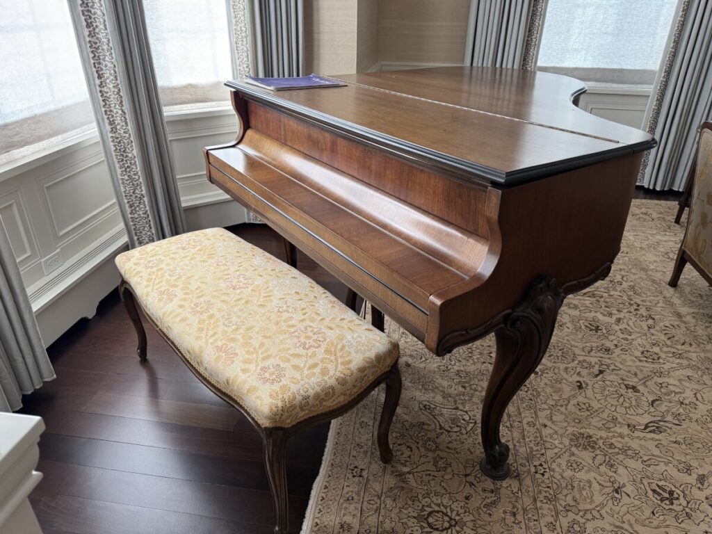 Restored antique grand piano with a custom‑upholstered bench displayed in the client’s home after refinishing.