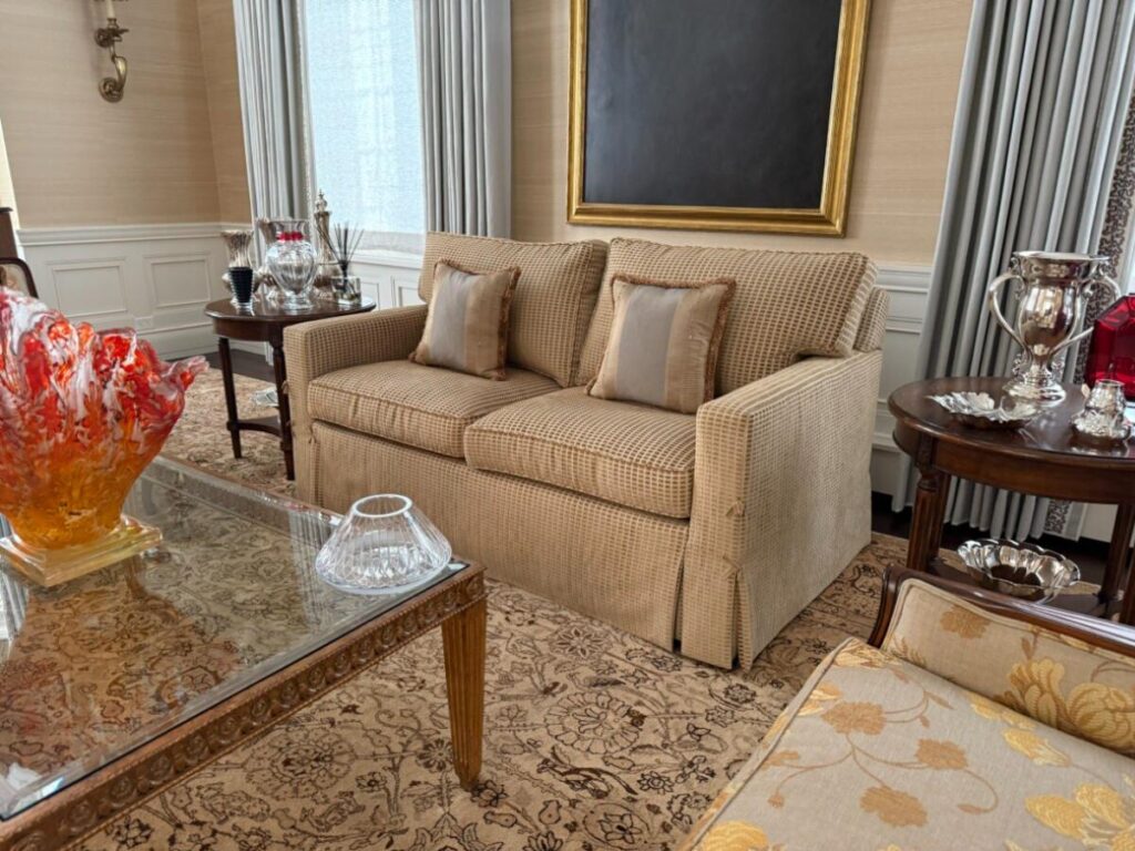 Restored Baker transitional-style sofa featuring a tailored checkered-pattern upholstery, dual plush back cushions with custom decorative pillows, and a traditional skirted base, shown after delivery in a luxury formal living room.