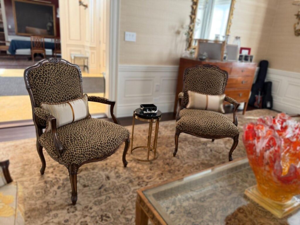 Living room with two leopard‑print armchairs, a round side table, and a glass coffee table with a red decorative sculpture.