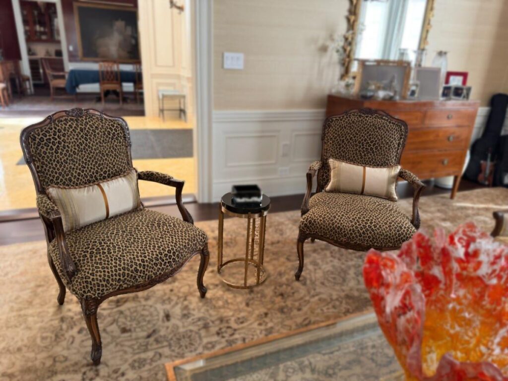 Pair of antique accent chairs reupholstered in luxury leopard‑print fabric, shown in the client’s home with throw pillows.