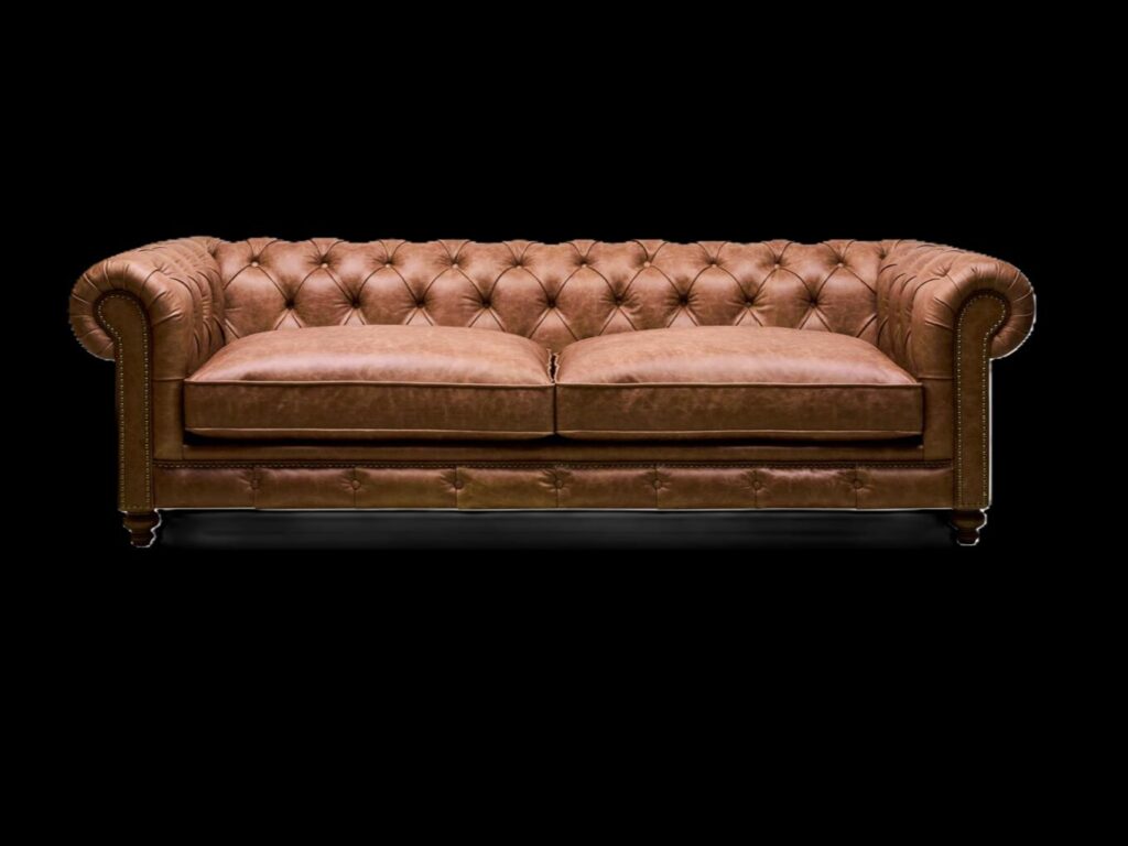 Handcrafted brown leather Chesterfield sofa with deep diamond tufting, rolled arms, and brass nailhead trim set against a black background.