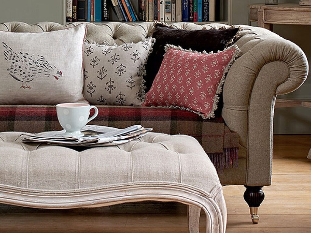 Handcrafted light grey tufted Chesterfield sofa featuring rolled arms and a matching oversized tufted ottoman with an elegant carved wood base.