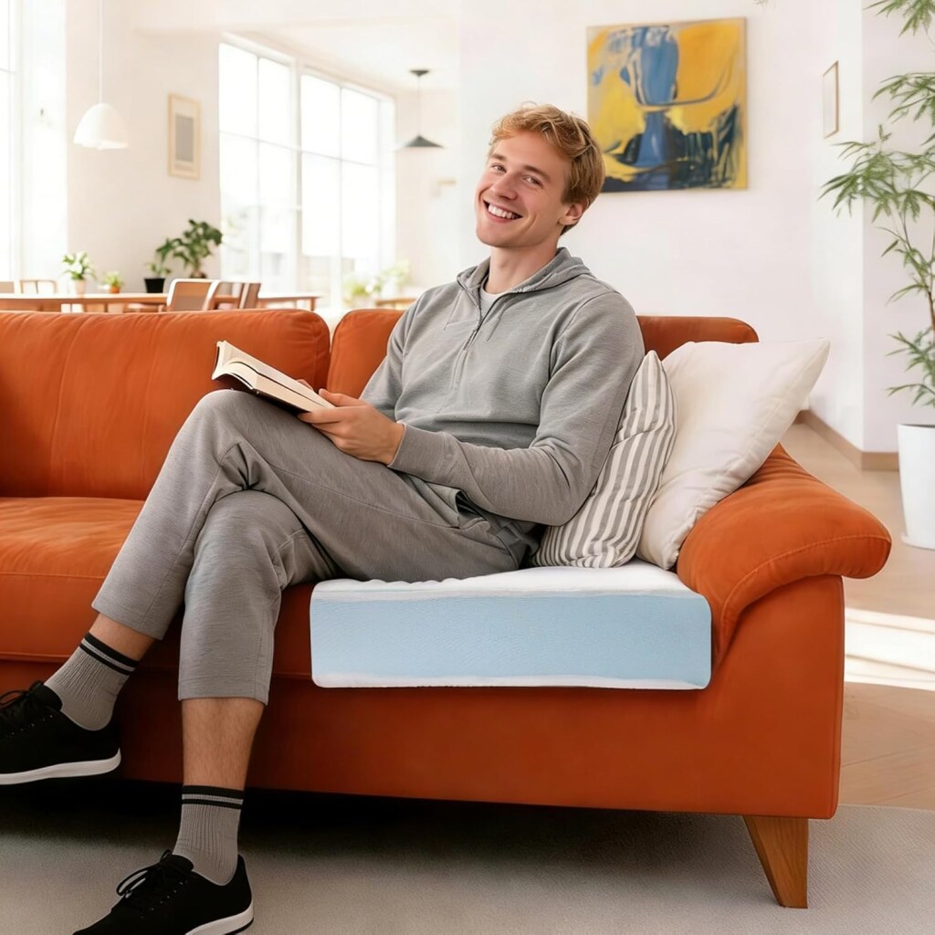 Person sitting on an orange sofa with a light blue replacement cushion on the seat, surrounded by striped pillows, plants, and large windows in a bright living room.