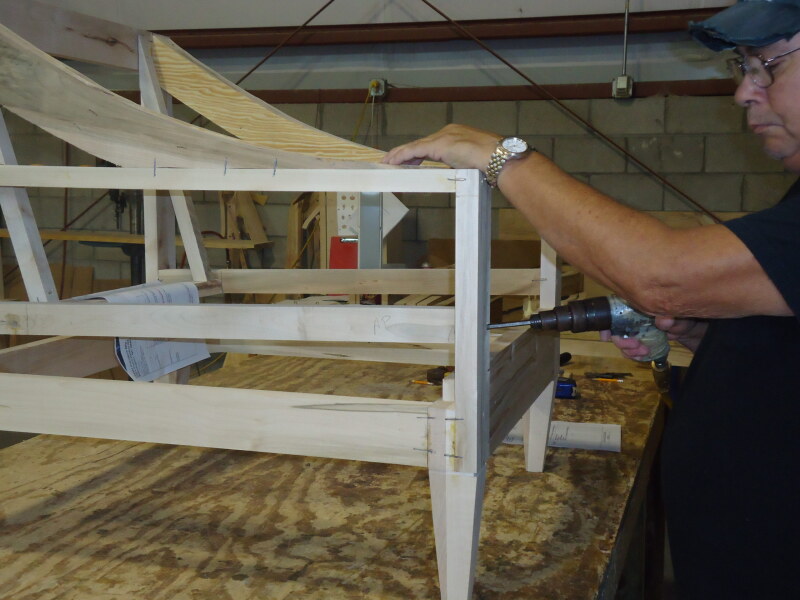 Person working on a wooden sofa frame on a workbench with tools and materials in the background.