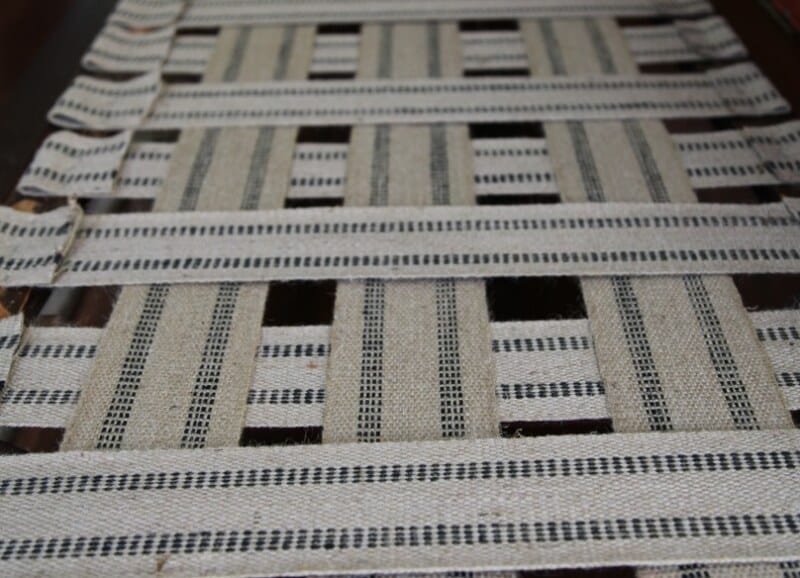 Interwoven beige and dark-striped webbing forming a crisscross support grid for upholstered furniture.