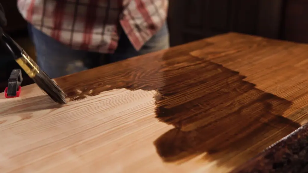Hand applying a dark wood finish with a brush onto a wooden surface.