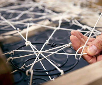 Hand tying white cords around metal coil springs in an upholstery frame.