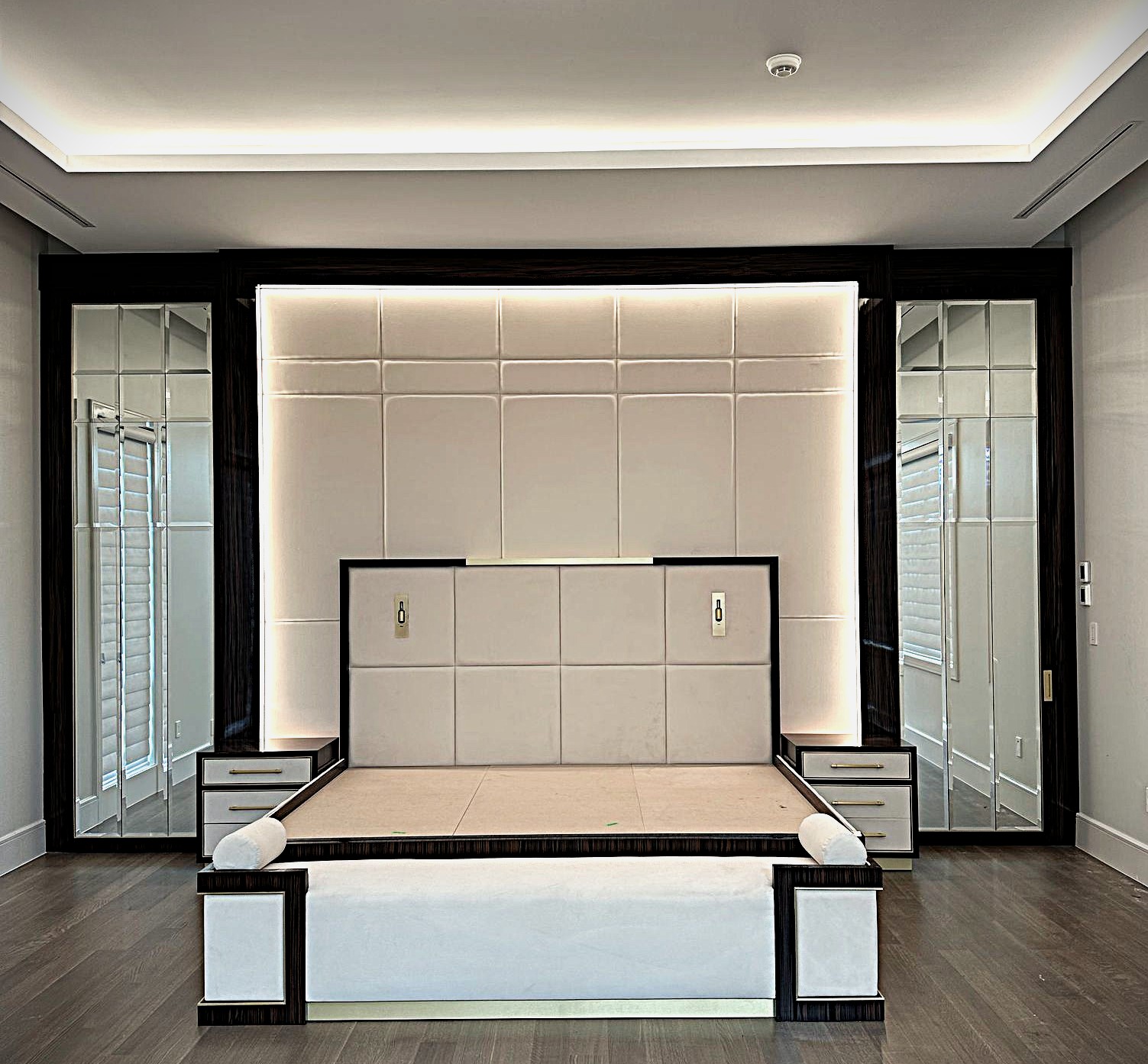 Custom architectural millwork and raw bed frame featuring integrated mirrors, led backlighting, and upholstered wall panels engineered by first class mastercraft.
