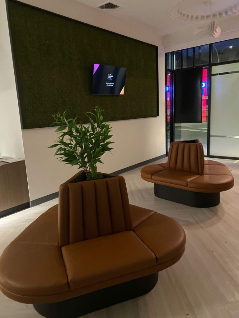 Custom tan leather island banquette seating featuring vertical channel tufting and an integrated central planter in a modern commercial lobby.