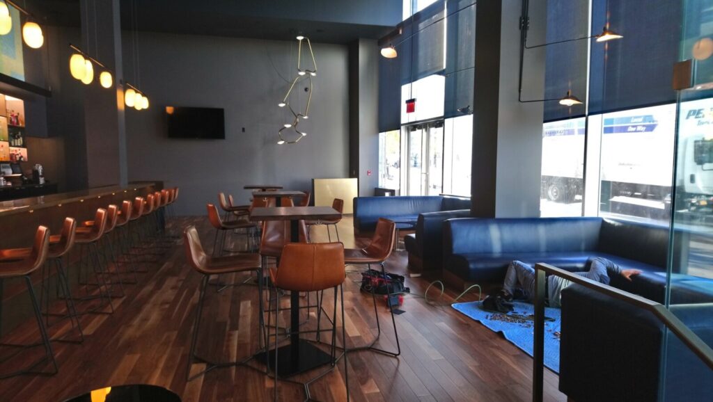An installation in progress for a commercial lounge, featuring custom blue leather banquettes fitted along large glass windows, alongside hightop tables and a bar with leather stools.
